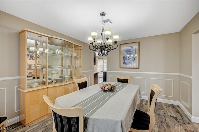 dining room featuring a chandelier, wood finished floors, visible vents, and a decorative wall