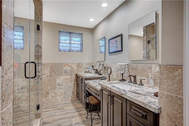 full bathroom featuring a stall shower, tile walls, two vanities, and a sink