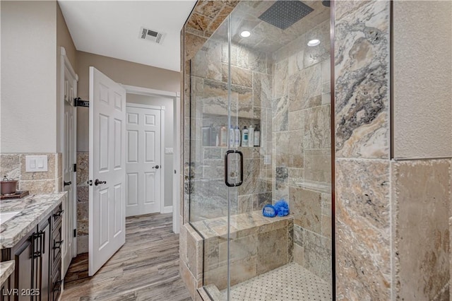 full bathroom with tile walls, a shower stall, visible vents, and wood finished floors