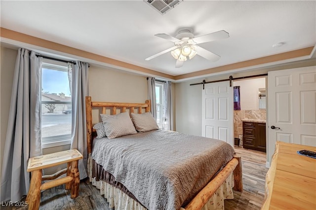 bedroom with wood finished floors, visible vents, multiple windows, and a barn door