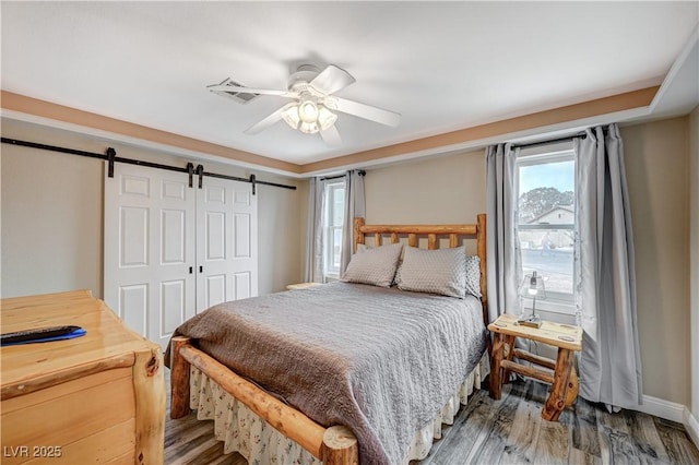 bedroom with a barn door, a closet, wood finished floors, and a ceiling fan