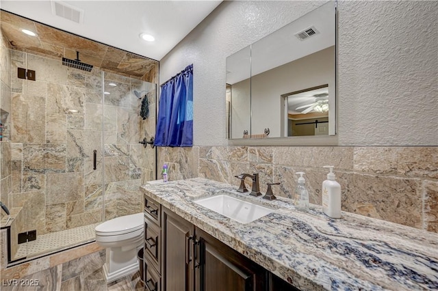 bathroom with toilet, a shower stall, visible vents, and tile walls