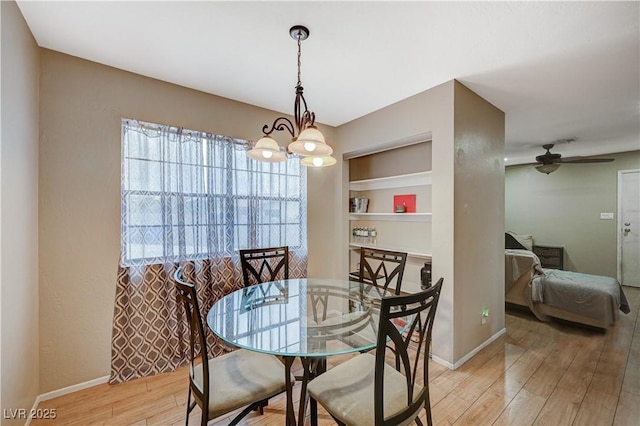 dining room featuring ceiling fan with notable chandelier, built in shelves, light wood-style flooring, and baseboards