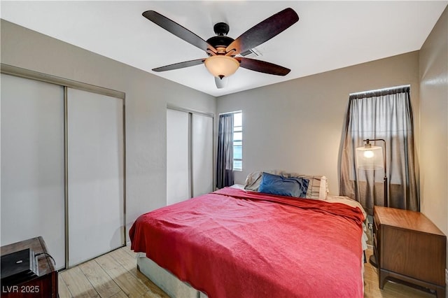 bedroom with light wood-style floors, ceiling fan, and multiple closets