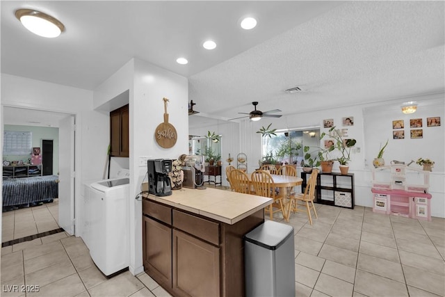 kitchen featuring light tile patterned floors, a ceiling fan, a textured ceiling, washer / dryer, and a peninsula