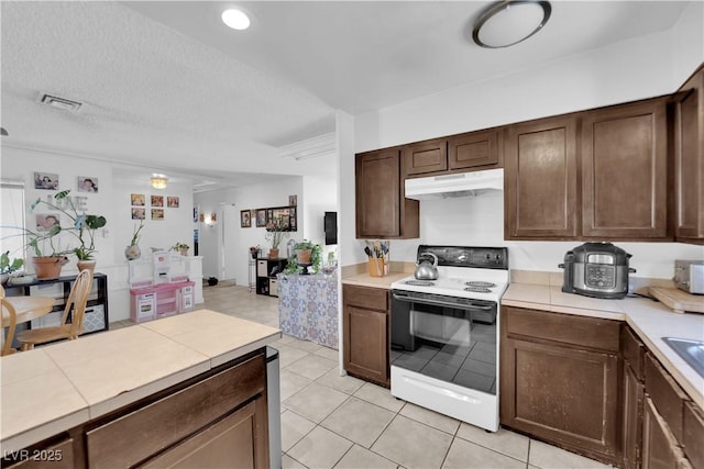 kitchen featuring dark brown cabinetry, tile counters, visible vents, white electric range, and under cabinet range hood