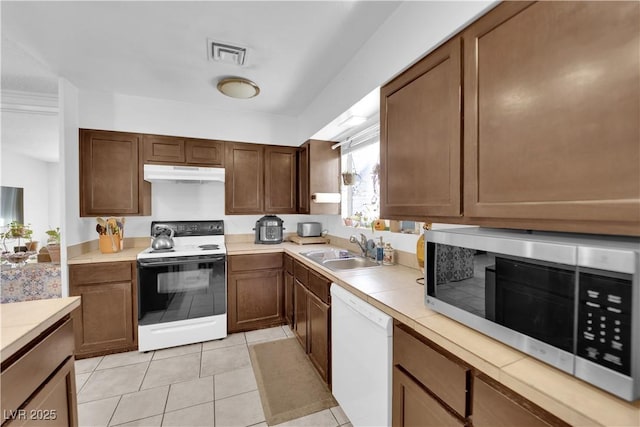 kitchen with light tile patterned floors, under cabinet range hood, white appliances, a sink, and visible vents