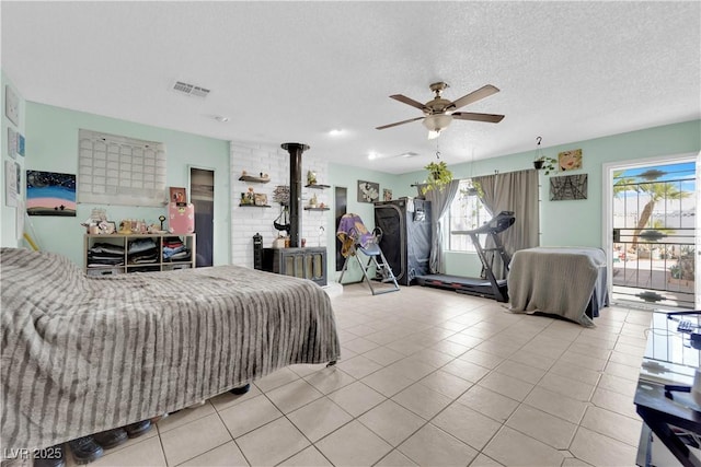 bedroom with visible vents, ceiling fan, a wood stove, a textured ceiling, and light tile patterned flooring