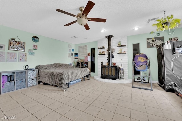 tiled bedroom featuring visible vents, ceiling fan, a textured ceiling, and a wood stove