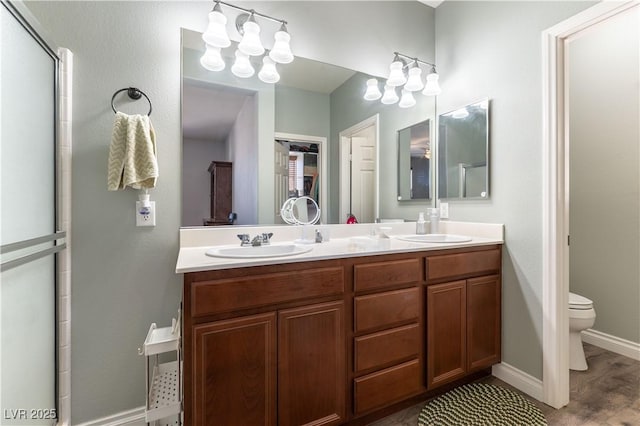 bathroom featuring toilet, double vanity, baseboards, and a sink