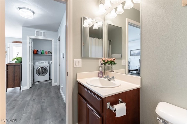 bathroom featuring toilet, wood finished floors, vanity, visible vents, and washer and clothes dryer