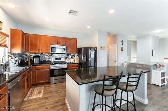 kitchen with stainless steel appliances, visible vents, dark wood-type flooring, a sink, and a kitchen island