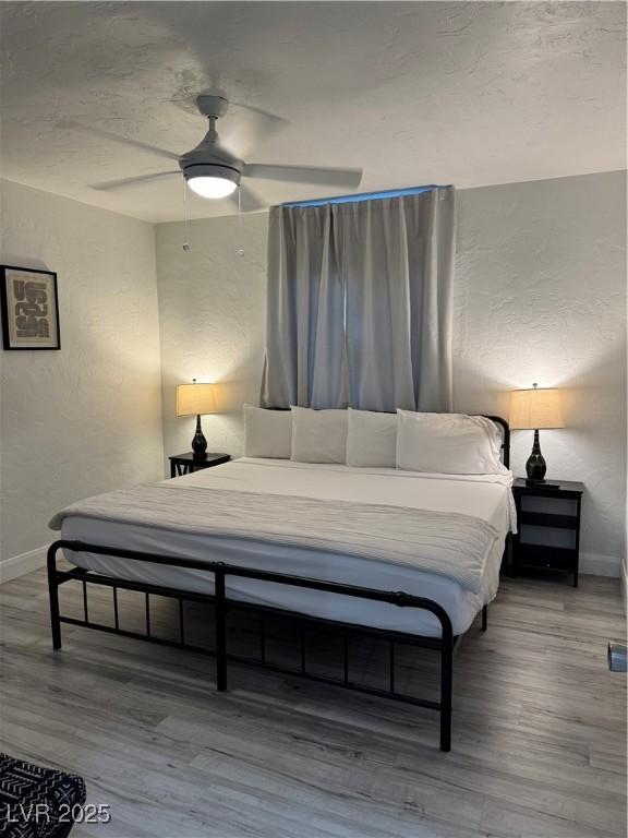 bedroom featuring a textured wall, wood finished floors, a ceiling fan, and baseboards