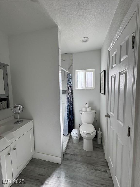 full bathroom with toilet, a shower with curtain, wood finished floors, a textured ceiling, and vanity