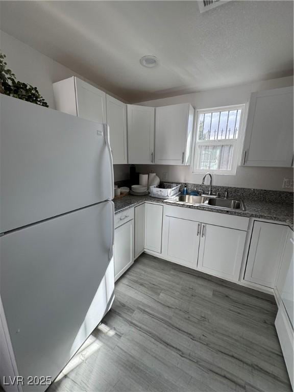 kitchen with dark countertops, light wood-style floors, freestanding refrigerator, white cabinets, and a sink