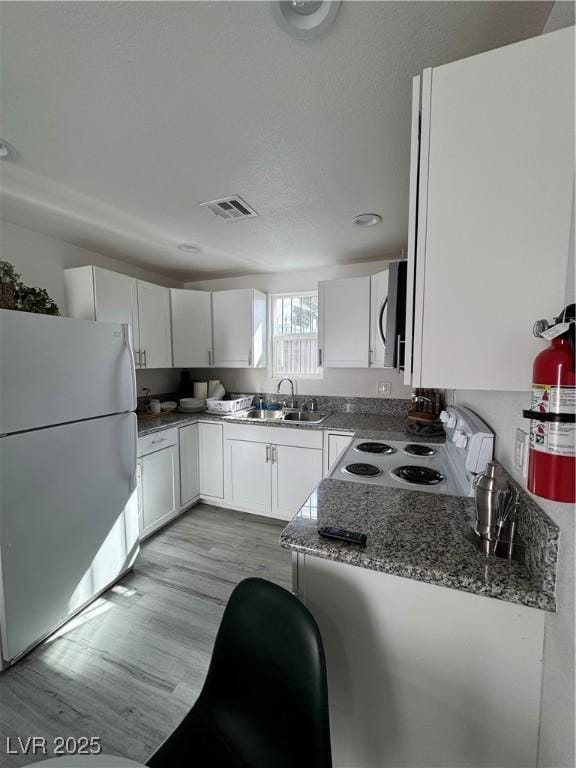 kitchen featuring white appliances, visible vents, white cabinets, light wood-type flooring, and a sink