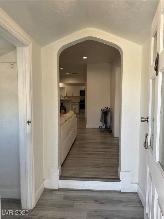 hall with baseboards, arched walkways, and wood finished floors