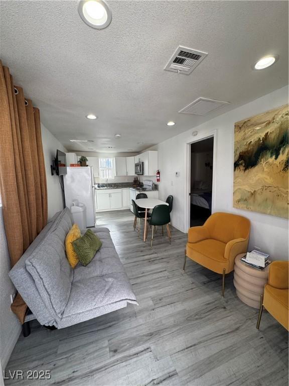 living area featuring a textured ceiling, light wood-type flooring, visible vents, and recessed lighting