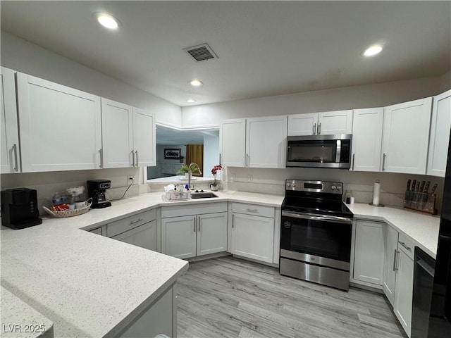 kitchen featuring recessed lighting, stainless steel appliances, a peninsula, a sink, and light countertops