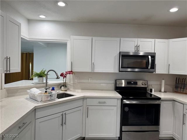 kitchen with light countertops, appliances with stainless steel finishes, a sink, and white cabinetry