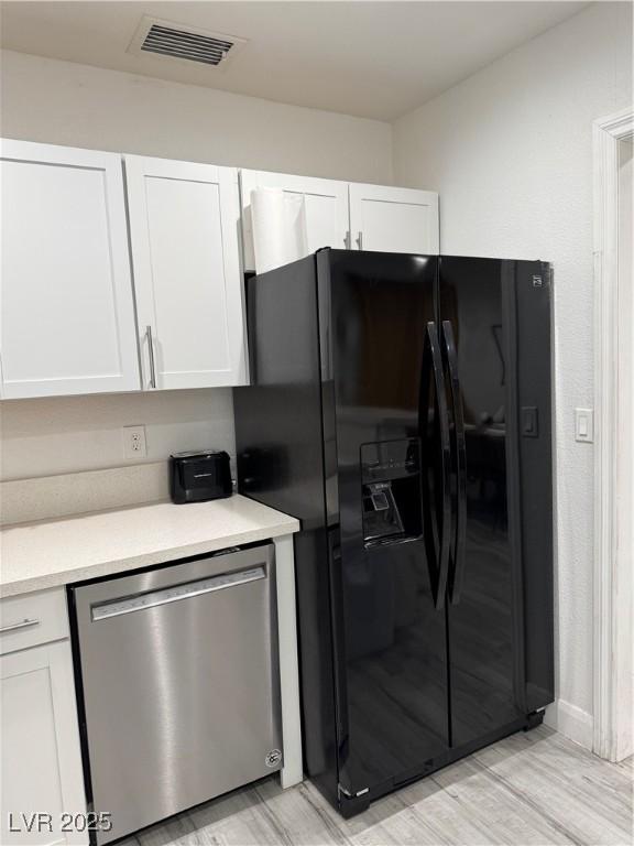 kitchen featuring light countertops, visible vents, black refrigerator with ice dispenser, white cabinetry, and dishwasher