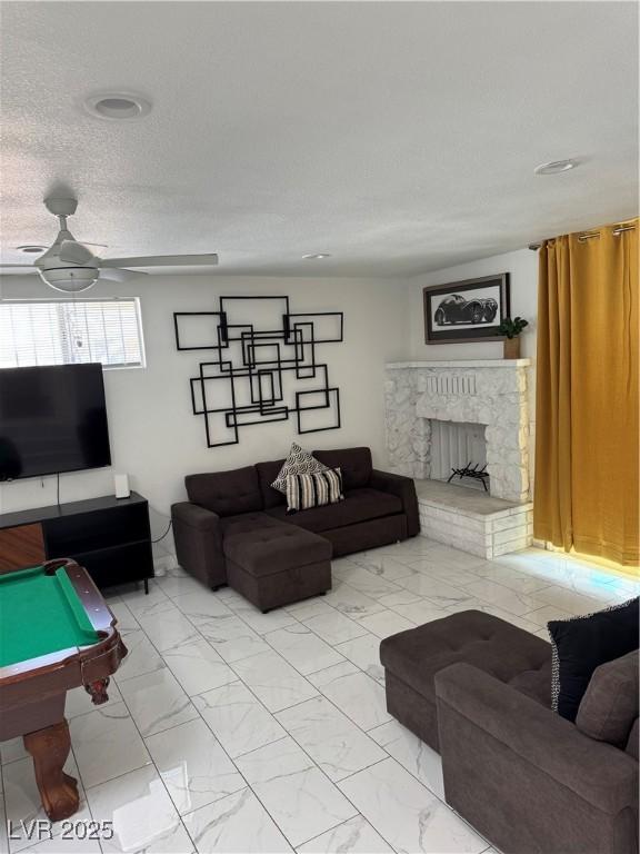 living area with a textured ceiling, marble finish floor, and a fireplace with raised hearth