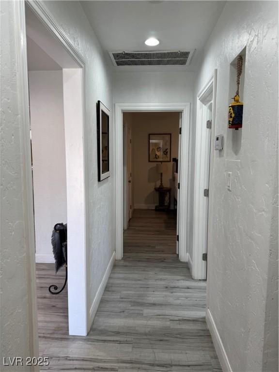 hallway featuring light wood-style flooring, visible vents, baseboards, and a textured wall