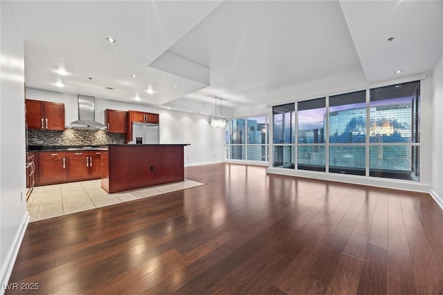 kitchen featuring wall chimney exhaust hood, dark countertops, light wood-style flooring, backsplash, and built in refrigerator