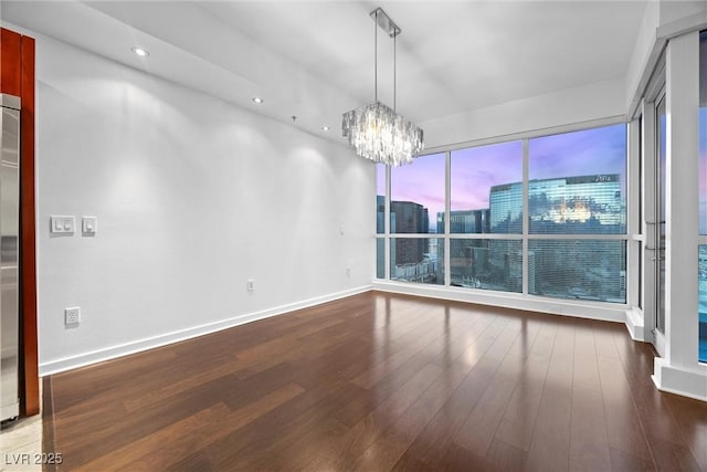 spare room featuring baseboards, hardwood / wood-style floors, recessed lighting, and an inviting chandelier