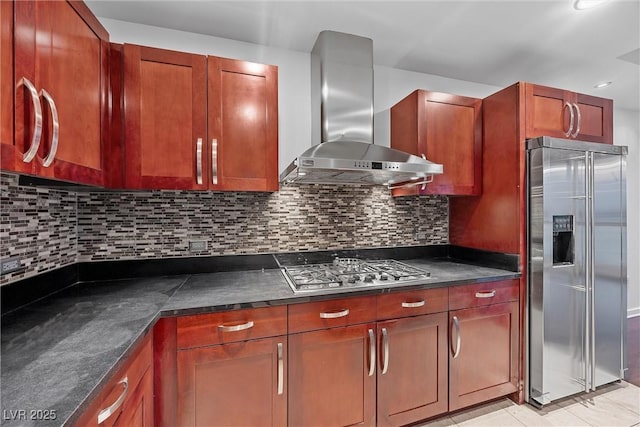 kitchen featuring light tile patterned floors, wall chimney range hood, appliances with stainless steel finishes, backsplash, and dark countertops