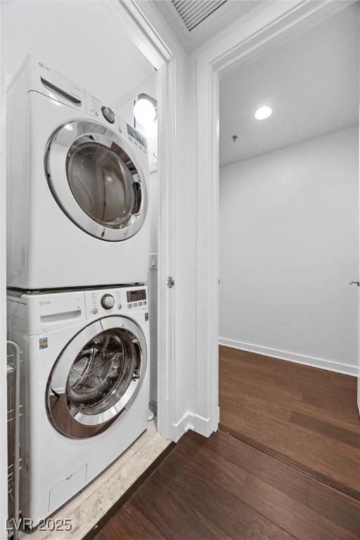 laundry room with laundry area, visible vents, baseboards, stacked washer / dryer, and wood finished floors