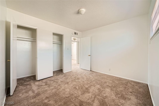 unfurnished bedroom featuring a textured ceiling, carpet floors, visible vents, and baseboards