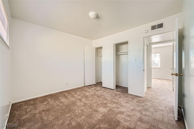 unfurnished bedroom with two closets, a textured ceiling, visible vents, and carpet flooring