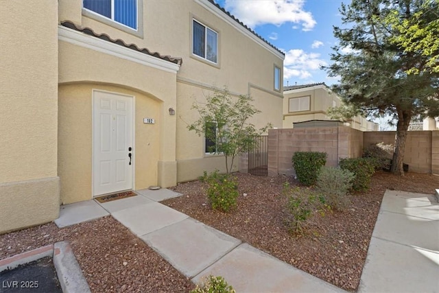 doorway to property featuring a tile roof, fence, and stucco siding