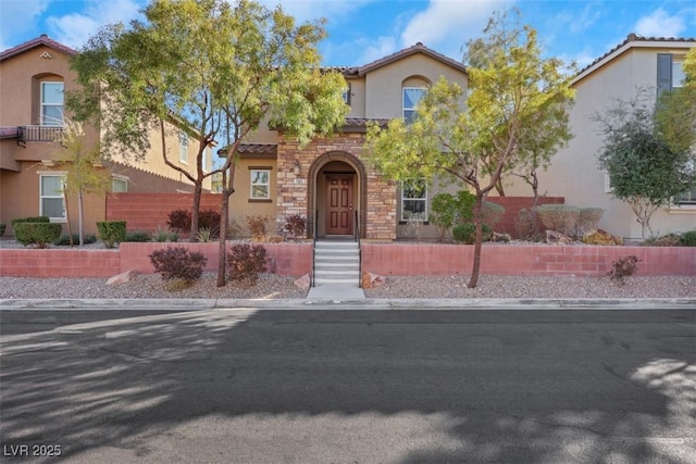 mediterranean / spanish home with stone siding, a tile roof, fence, and stucco siding