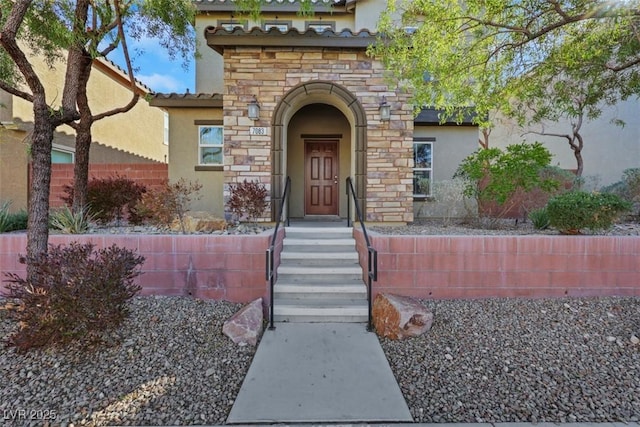 entrance to property featuring stone siding, a tiled roof, and stucco siding