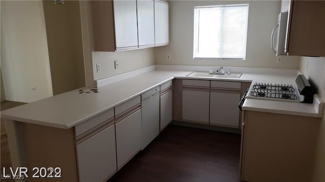 kitchen featuring white dishwasher, a peninsula, a sink, light countertops, and dark wood finished floors