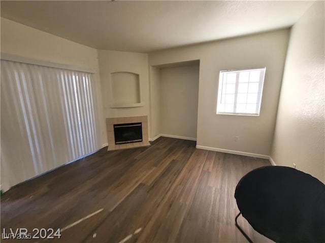 unfurnished living room featuring dark wood-type flooring, baseboards, and a tiled fireplace