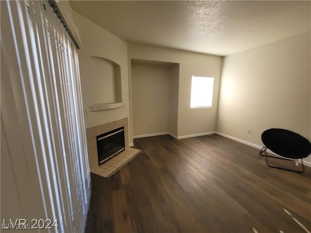 unfurnished living room with dark wood-style floors, a textured ceiling, baseboards, and a tiled fireplace