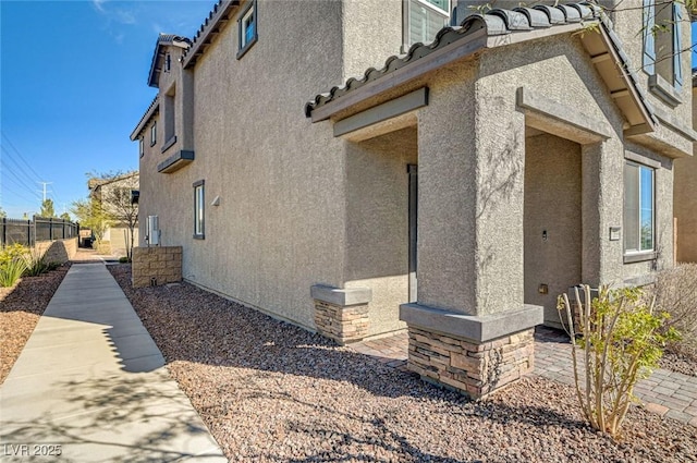 view of home's exterior with a tile roof, fence, and stucco siding