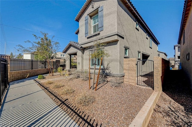 view of side of home with a tile roof, fence private yard, a gate, and stucco siding