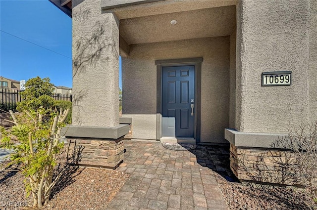 view of exterior entry with fence and stucco siding