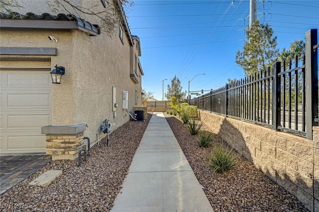 view of home's exterior featuring a garage, cooling unit, fence, and stucco siding