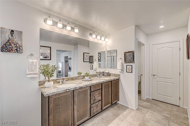 full bathroom with a textured ceiling, double vanity, a sink, and baseboards