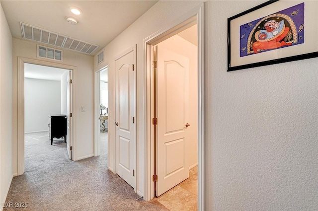 hall featuring baseboards, visible vents, and light colored carpet