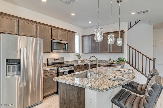 kitchen featuring visible vents, light stone counters, a breakfast bar area, stainless steel appliances, and a sink