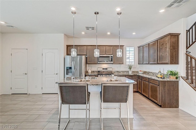 kitchen with appliances with stainless steel finishes, visible vents, an island with sink, and light stone countertops