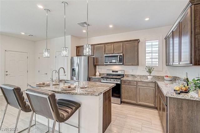 kitchen featuring appliances with stainless steel finishes, light stone counters, a kitchen breakfast bar, a kitchen island with sink, and a sink