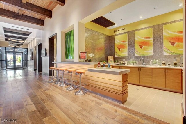 kitchen featuring light wood finished floors, decorative backsplash, beamed ceiling, light countertops, and a sink