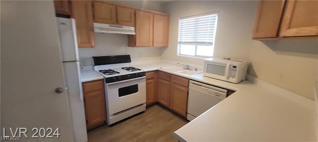 kitchen featuring light wood finished floors, light countertops, a sink, white appliances, and under cabinet range hood